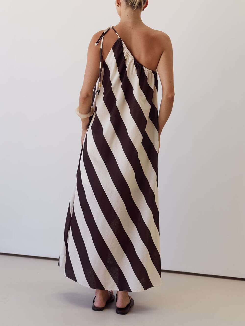 Vestido maxi elegante às riscas, estampado, com um ombro descoberto, laço na cintura e bolsos laterais